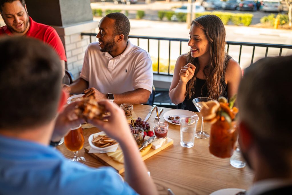 Group of adults sharing cheese board and drinking cocktails on the front patio at Red Door Lakeland, FL