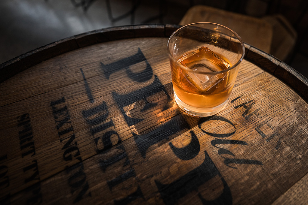 glass with ice and bourbon on a distillery barrel